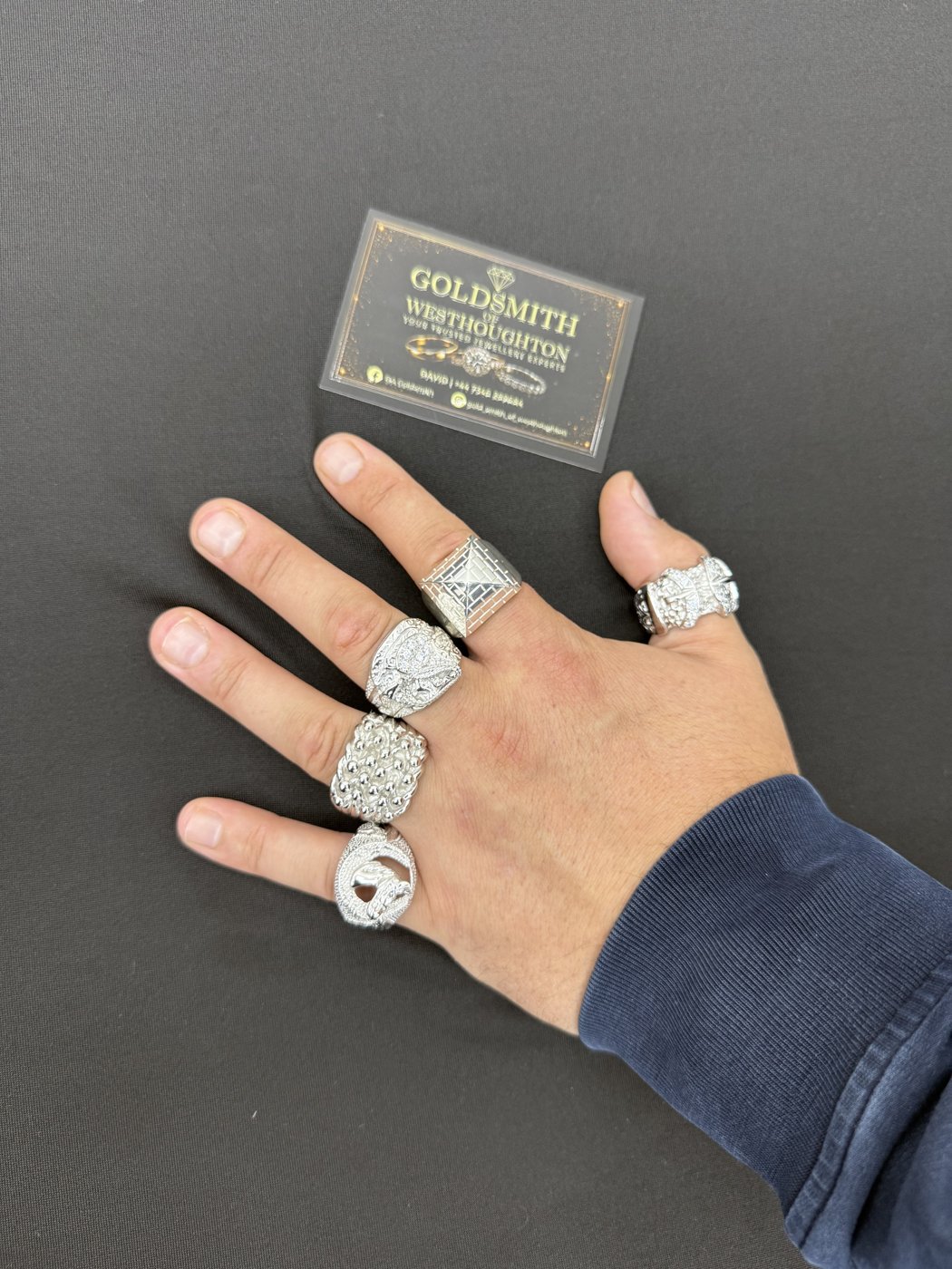 Several rings worn on a hand beside a DA Goldsmith card